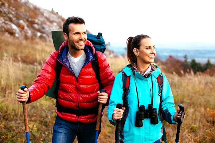Smiling couple with hiking poles and backpacks on a grassy mountain trail