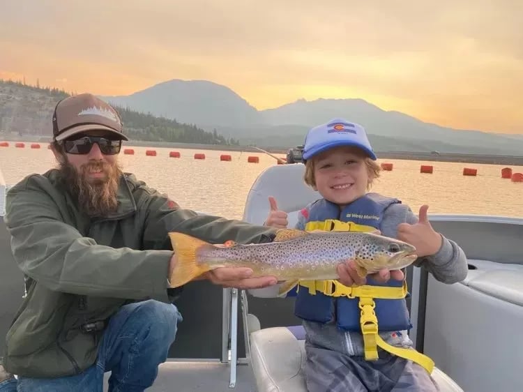 Man and boy holding a brown trout on a boat at sunset