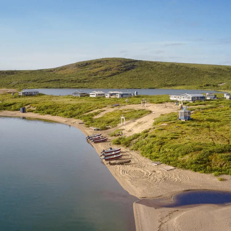 Aerial view of Peterson's Point Lake Lodge with guest cabins, sandy beach, and boats along the lake shore.