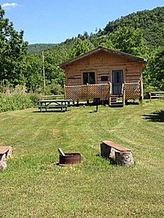 Two log cabins in a grassy field with a forested hill