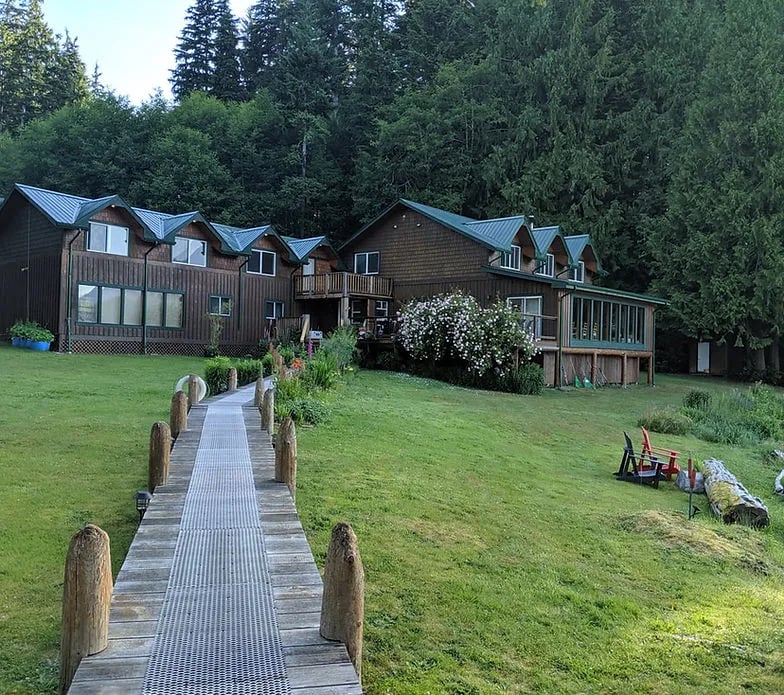 Wooden pathway leading to the main lodge building with green roofs and flowering bushes