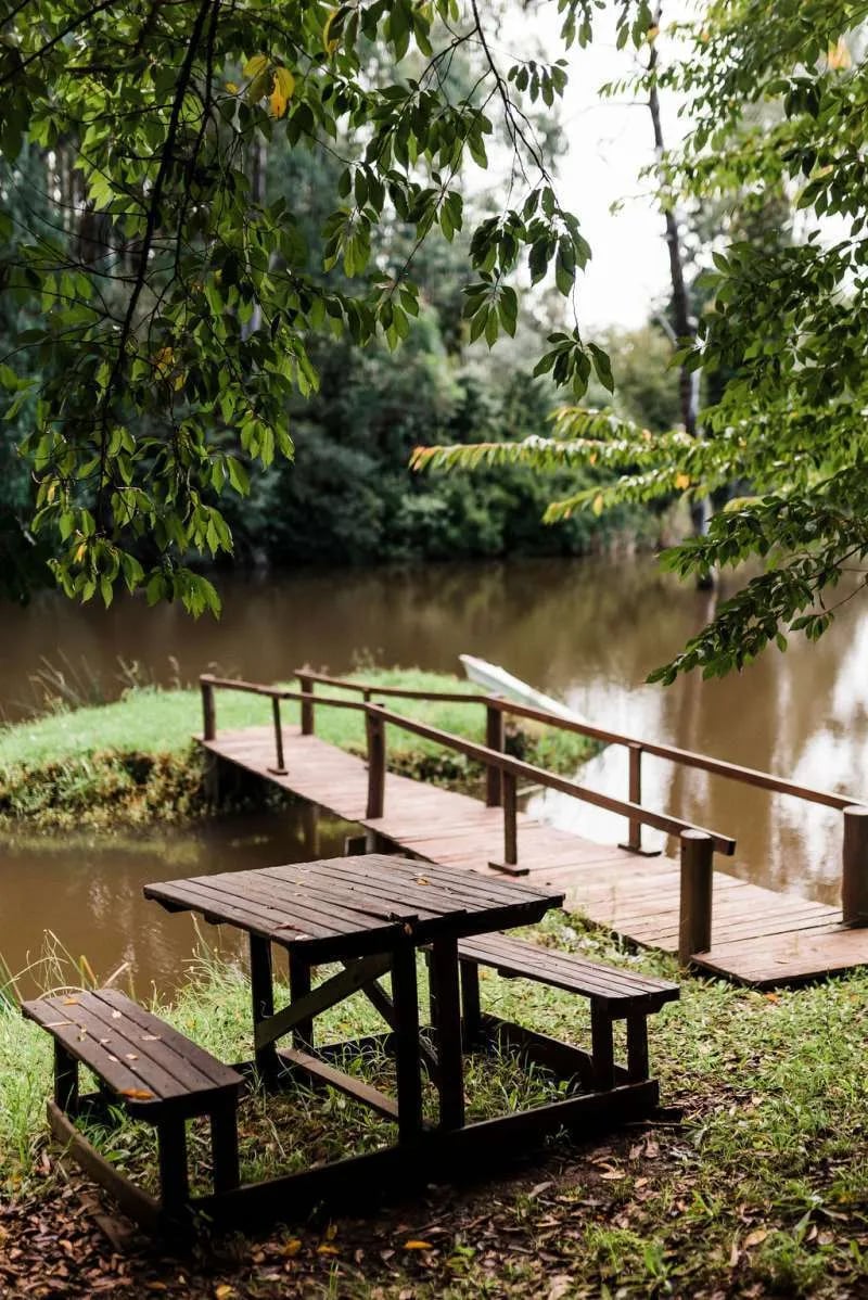 Wooden picnic table and a small wooden bridge over a stream, surrounded by trees.
