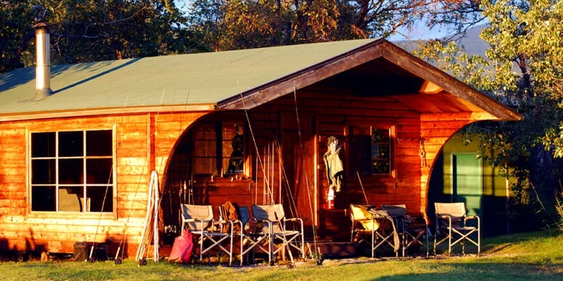 Wooden lodge cabin with a green roof and chairs on the front porch.