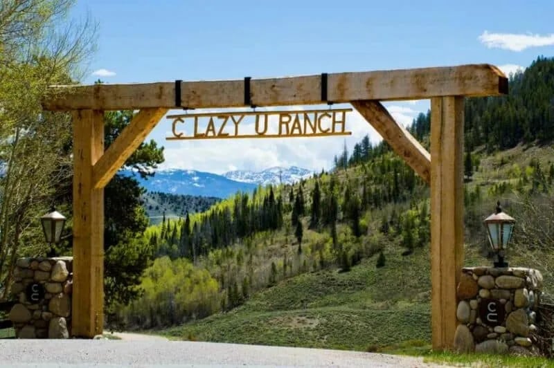 Rustic wooden entry gate to C Lazy U Ranch with mountains in the background.