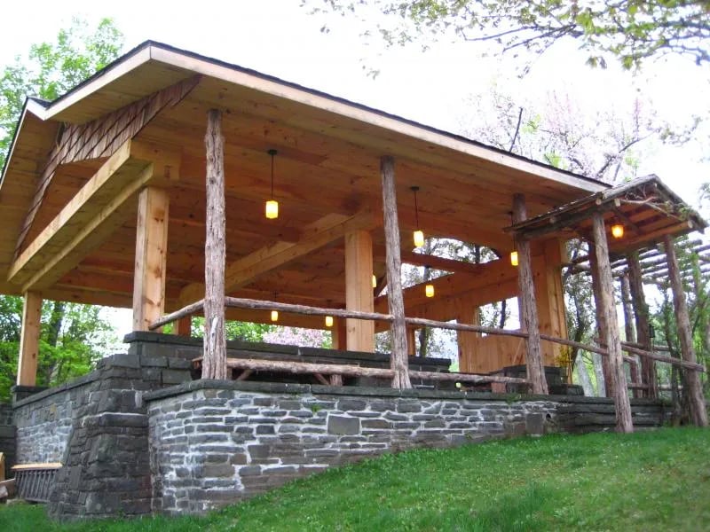 Close-up of a rustic wooden gazebo with a bench, overlooking a distant lake and mountains.