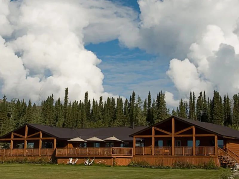 Main lodge building with a large deck and green lawn under a cloudy sky