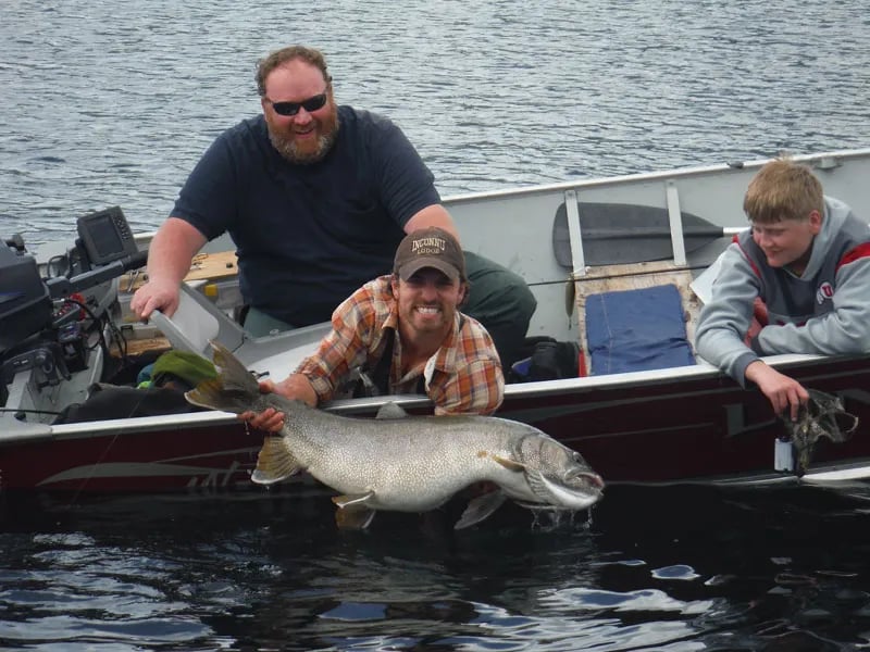 Three anglers in a boat holding a massive lake trout