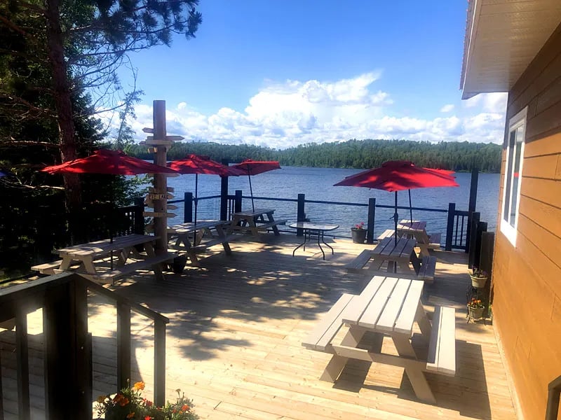 Outdoor wooden deck with picnic tables and red umbrellas overlooking a serene lake
