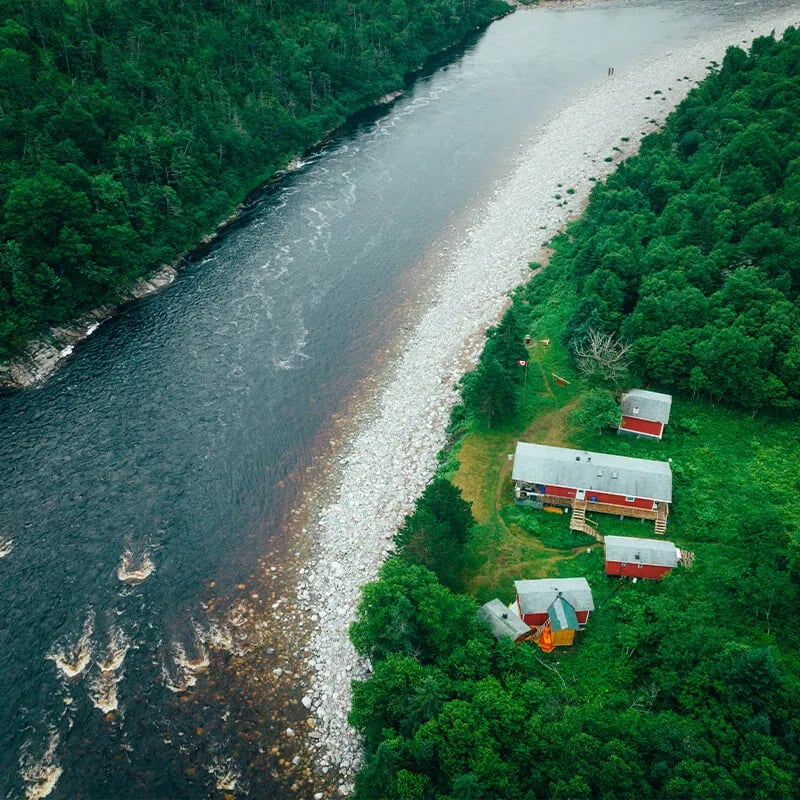Aerial view of red-roofed lodge buildings along a wide river with a gravel bar