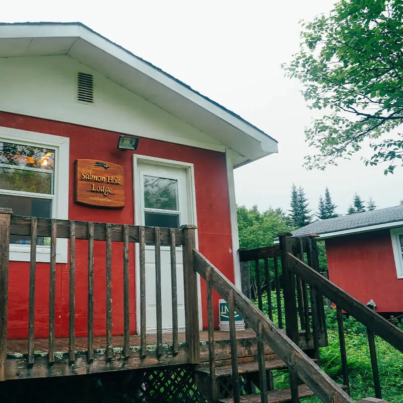 Red cabin exterior with a white door and a wooden Salmon Hole Lodge sign
