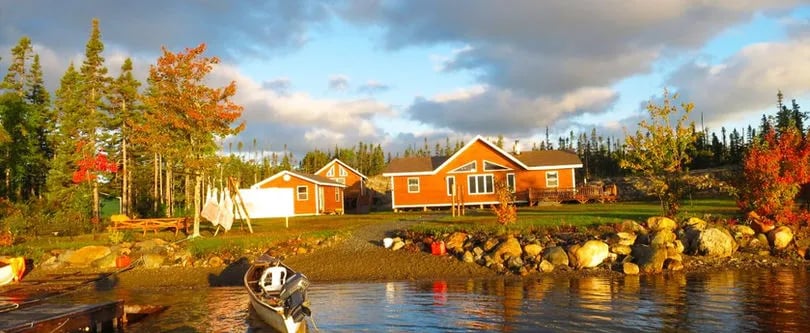WhiteCliff Lodge on a lake shore at golden hour with a canoe in the foreground.