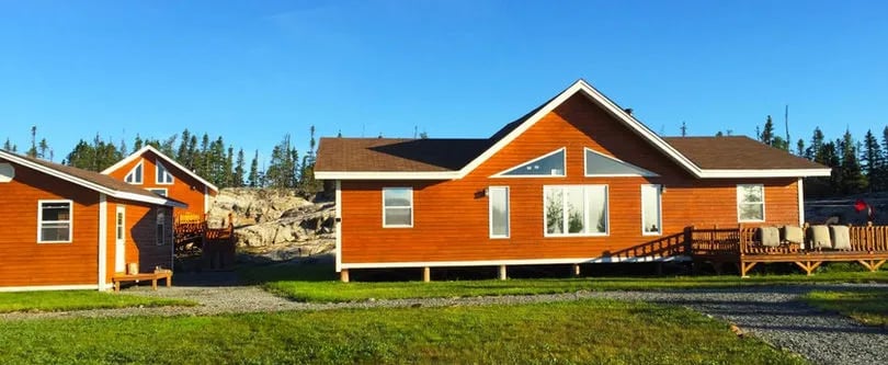 Main lodge building and a smaller cabin on a sunny green lawn.