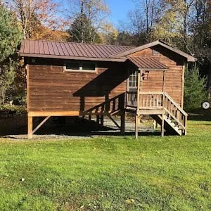 Owners standing behind a wooden "Creekside" sign with a cabin in the background
