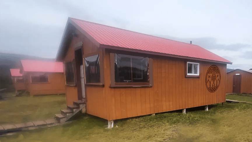 Exterior of a rustic brown cabin with a red roof and small porch