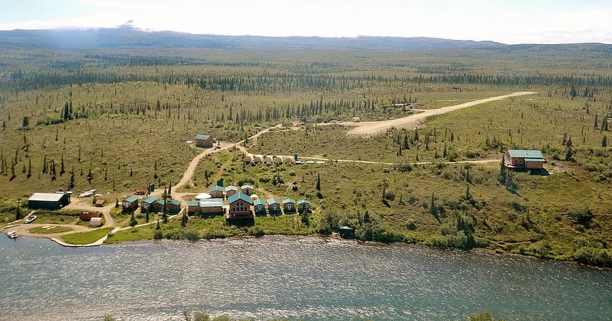 Aerial view of a remote lodge compound with cabins, a main building, river, and airstrip