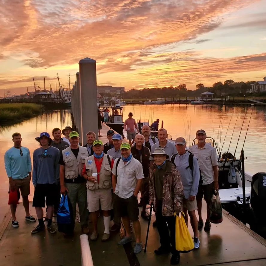 Group of anglers gathered on a dock at sunset with boats in the marina