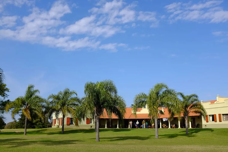 Aerial view of the lodge compound with main buildings, pool, and surrounding green fields