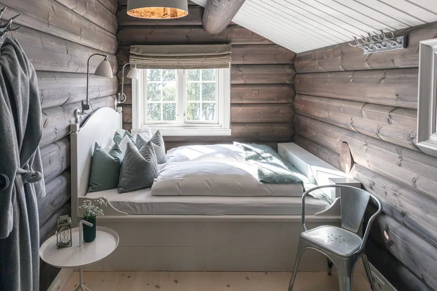 Rustic bedroom with log walls, a single bed with green pillows, and a window