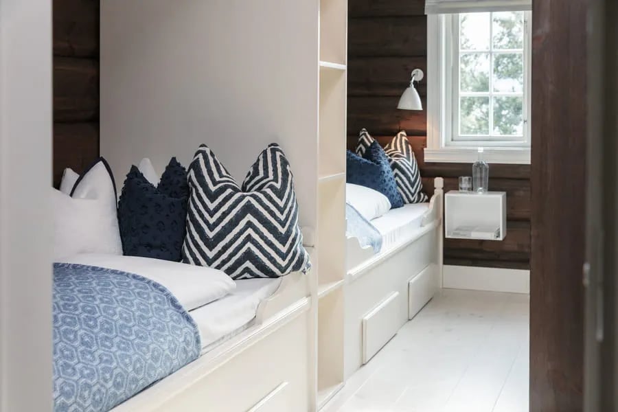 Twin beds with blue and white patterned pillows in a cozy log-walled room