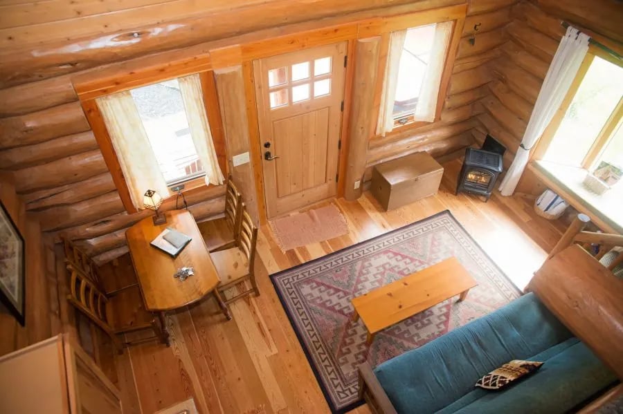 Large log cabin exterior with a wide covered porch and a green roof, set in a forest.
