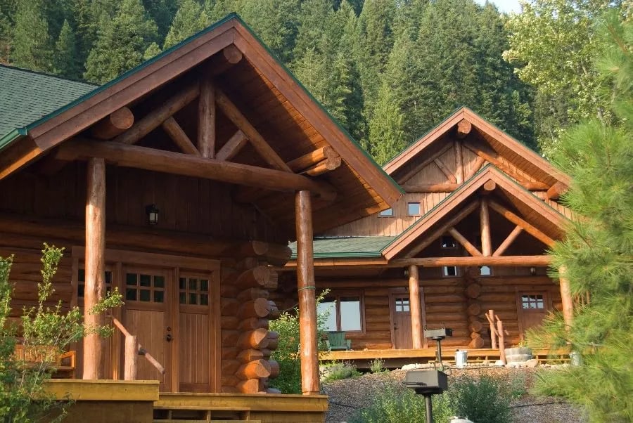 Rustic log cabin exterior with a green roof and front porch surrounded by trees.
