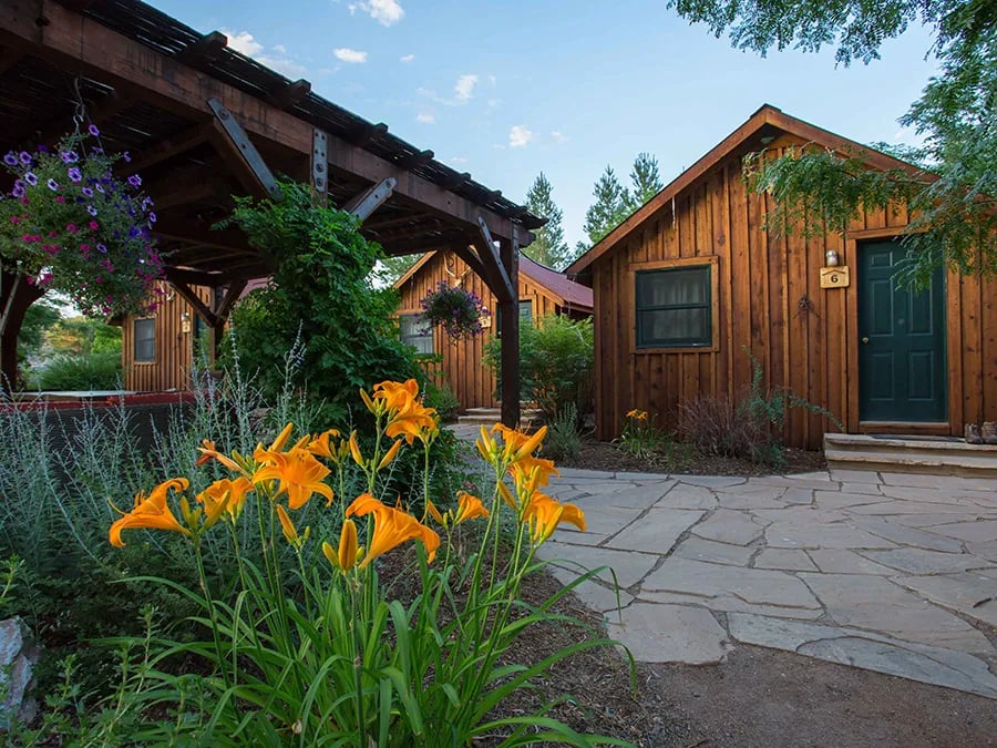 Rustic wooden cabins with a stone path and orange daylilies in the foreground.