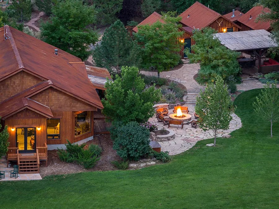 Aerial view of a lodge complex with multiple cabins, green lawns, and a fire pit area.