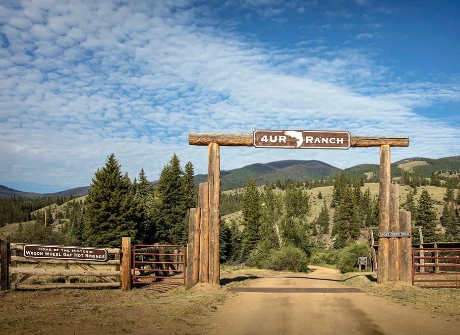 Rustic log entrance gate to 4UR Ranch under a blue sky.