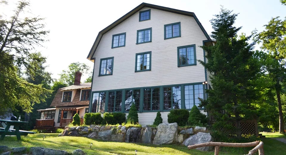 Large white multi-story lodge building with green window trim, surrounded by green trees under a bright sky