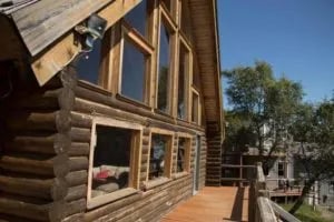 Side exterior of the main log lodge building with a long wooden deck and large windows.