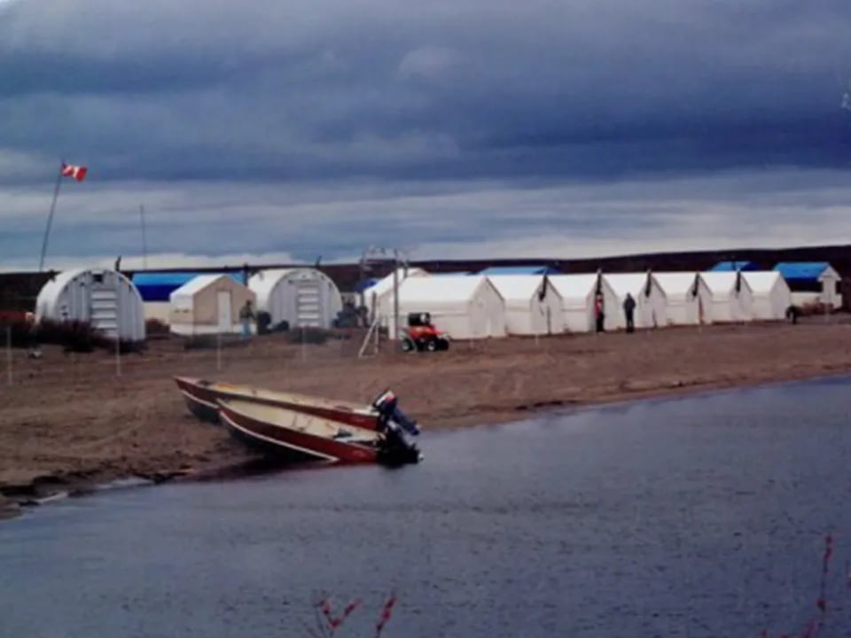 Row of white tent cabins on a sandy shore with a small boat in the foreground