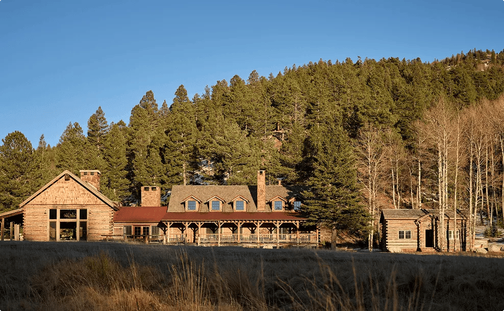 Large rustic lodge building nestled at the base of a pine-covered mountain